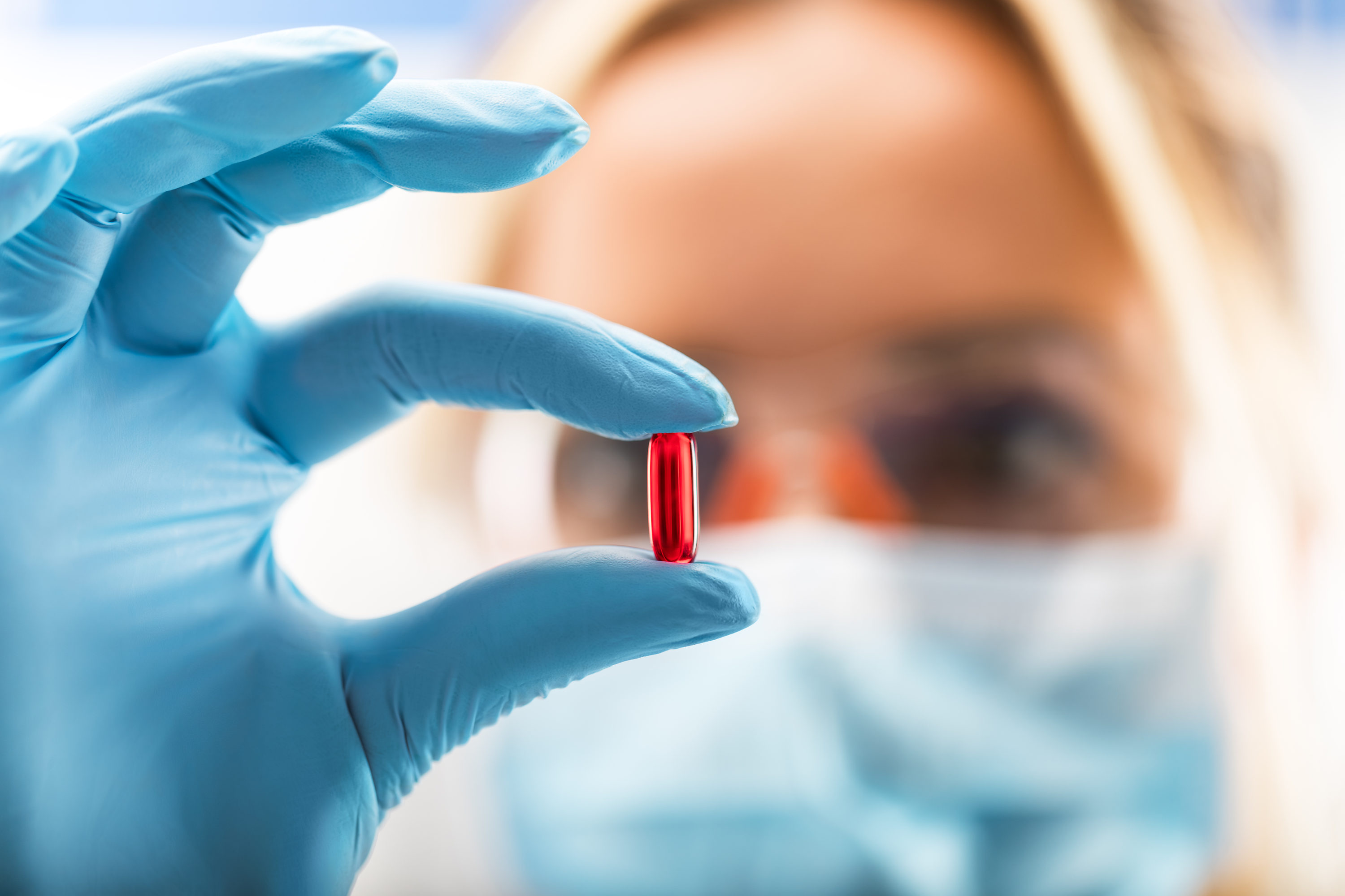 woman holding shiny red pill wearing blue gloves