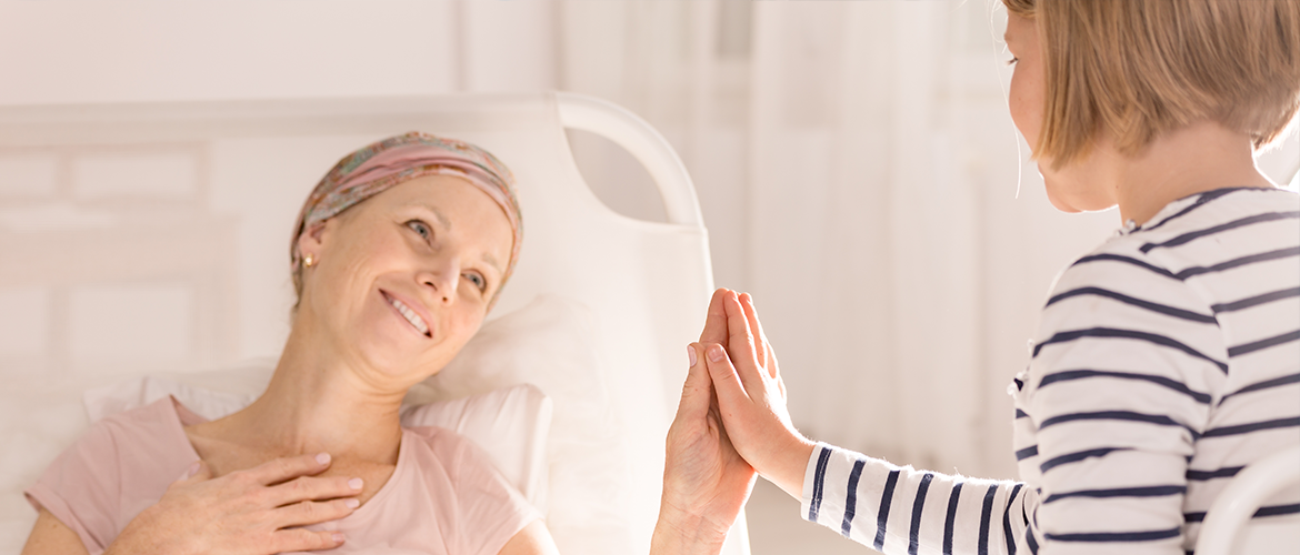 female cancer patient in bed holding hands with her young daughter