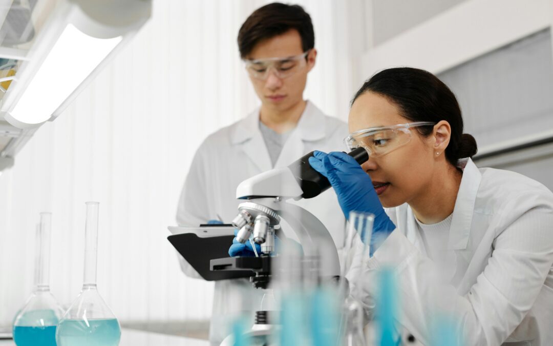 two scientists in a lab looking into a microscope at cancer cells