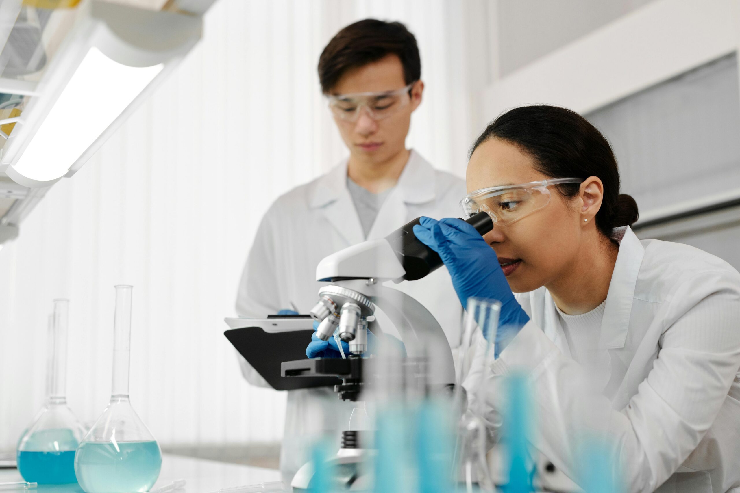 two scientists in a lab looking into a microscope at cancer cells